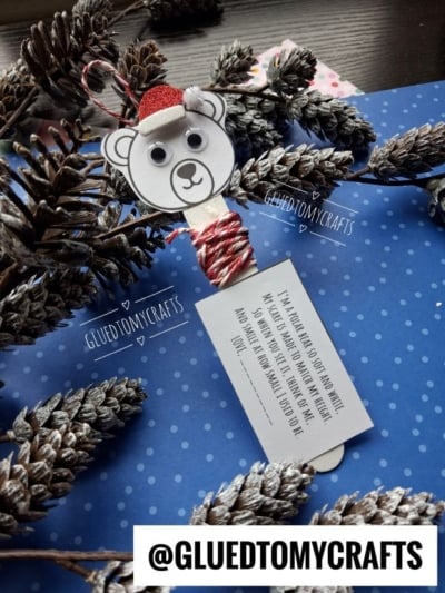 A craft of a polar bear head with a red Santa hat on a popsicle stick, tied with red and white string to a card printed with a poem about a polar bear.