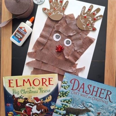 A handmade reindeer craft made from paper handprints and torn brown paper strips, displayed with glue, brown paper, and two Christmas childrens books.