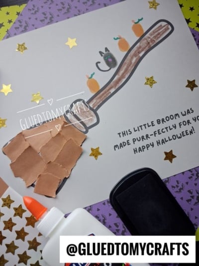 A DIY Halloween craft featuring a hand-drawn broom with paper-collage bristles, three orange thumbprint pumpkins, and one black thumbprint cat, with the text: This little broom was made purr-fectly for you! Happy Halloween!.