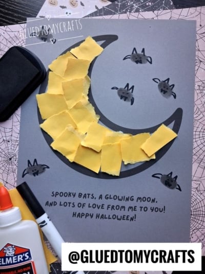 Halloween craft on gray paper featuring a crescent moon made of torn yellow paper, surrounded by small bat thumbprints with hand-drawn wings, and the printed text, Spooky bats, a glowing moon, and lots of love from me to you! Happy Halloween!.