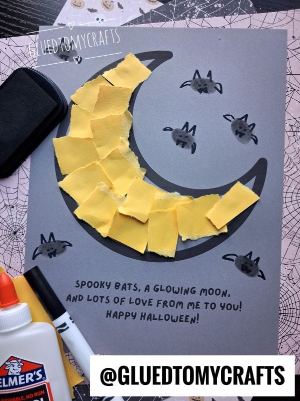 Halloween craft on gray paper featuring a crescent moon made of torn yellow paper, surrounded by small bat thumbprints with hand-drawn wings, and the printed text, Spooky bats, a glowing moon, and lots of love from me to you! Happy Halloween!.
