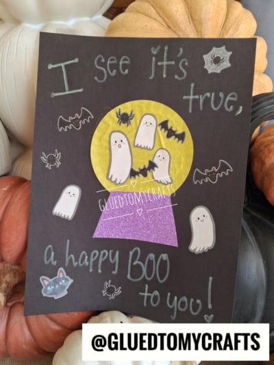 A handmade Halloween card with the text I see it’s true, a happy BOO to you! surrounding a crystal ball illustration containing three ghosts and a bat, perfect for Halloween crafts for kids.