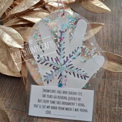 A clear plastic handprint ornament decorated with a snowflake and glitter, attached to a card with a poem about watching children grow.