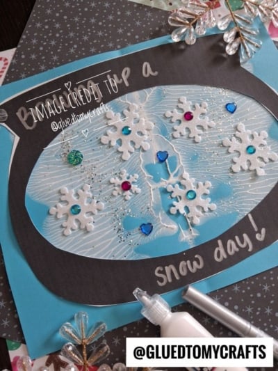 A handmade greeting card featuring a paper snow globe containing white glittery snowflakes and small colorful gems, with the handwritten text Brrr... its a snow day! on a black frame.