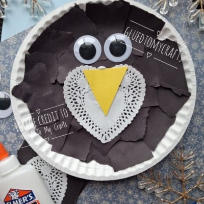 Paper plate craft of an owl made with torn black paper, a white paper doily, a yellow triangle beak, and two googly eyes.