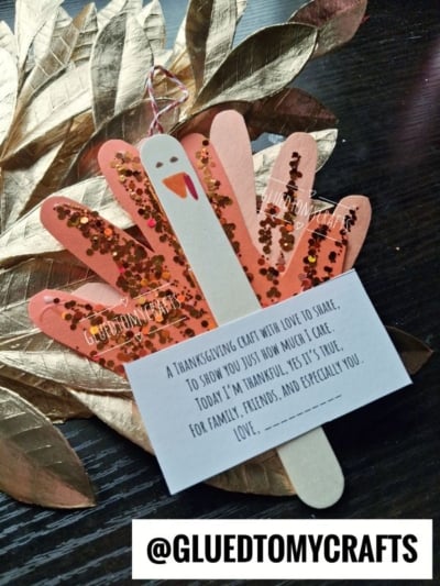A popsicle stick turkey craft with glittery paper feathers, attached to a card with a Thanksgiving poem.