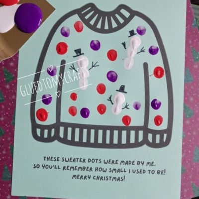 A light green sheet featuring an outline of a sweater decorated with painted dots and three small finger-painted snowmen, with text reading, These sweater dots were made by me, so youll remember how small I used to be! Merry Christmas!.
