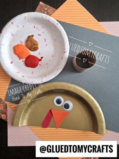 A gold paper plate decorated to look like a turkey, with a white plate containing drops of orange, red, and gold paint nearby.
