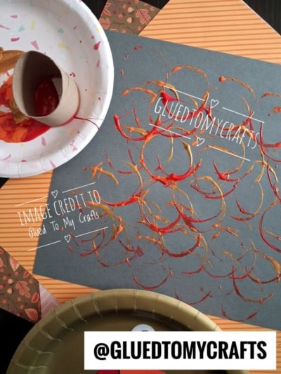 A sheet of black paper featuring a pattern of orange, red, and gold paint circles made by stamping with a cardboard tube.