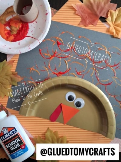 A paper plate turkey craft with googly eyes and orange beak, next to a paper plate with red and orange paint used for stamping on gray paper.